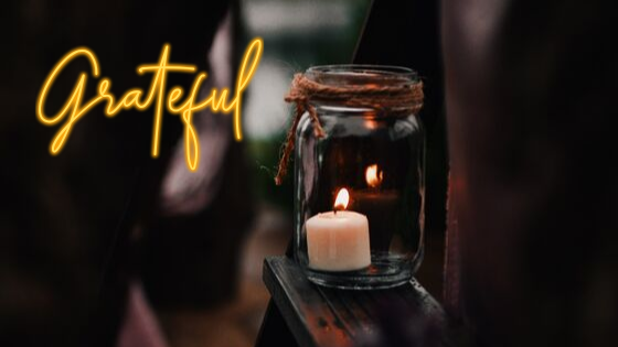 Płonąca świeczka w słoiku postawionym na desce. Z lewego boku napis: Grateful - wdzięczność